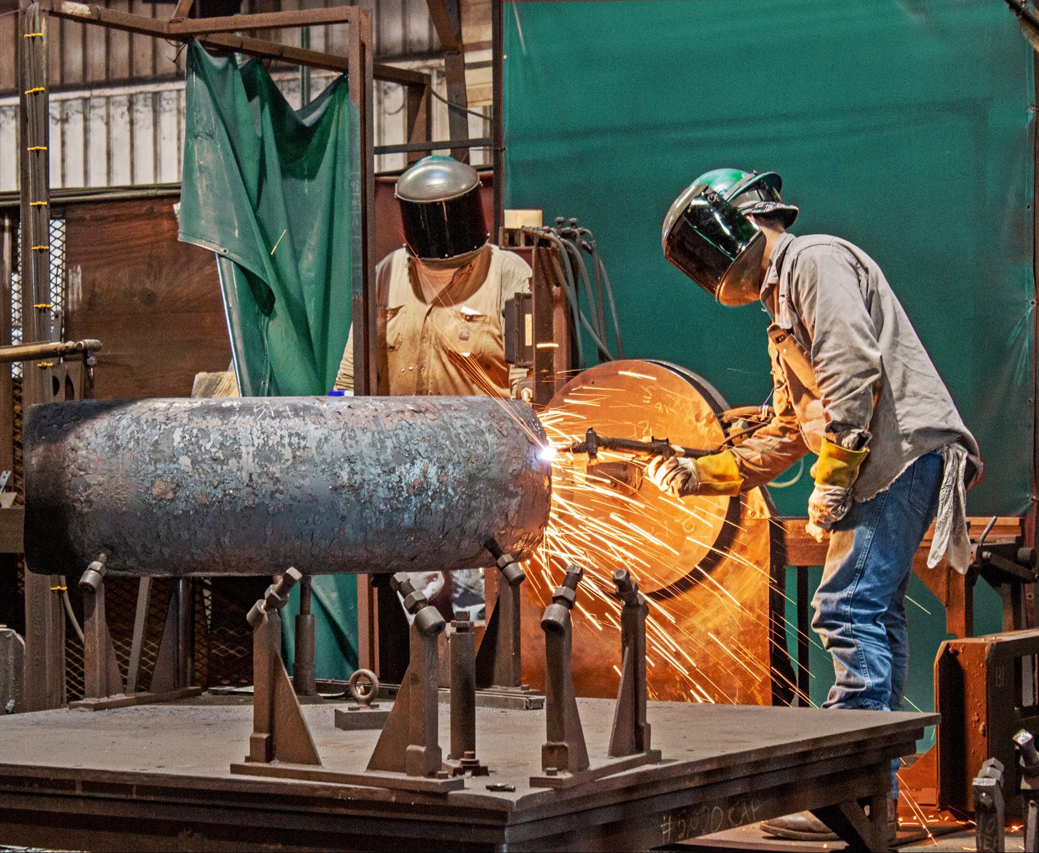 Workers in protective gear weld a large carbon fitting.