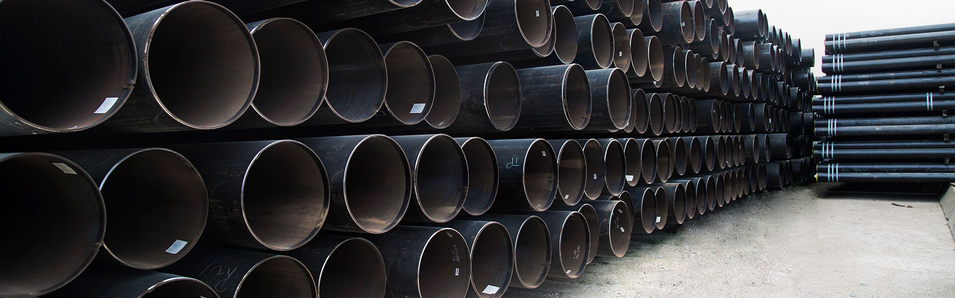 Large stacks of carbon steel pipe in a distribution yard.