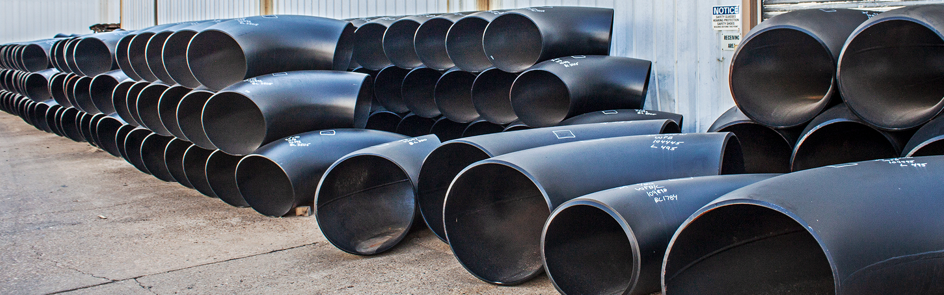 Large carbon steel fittings arranged in stacks outside a warehouse.