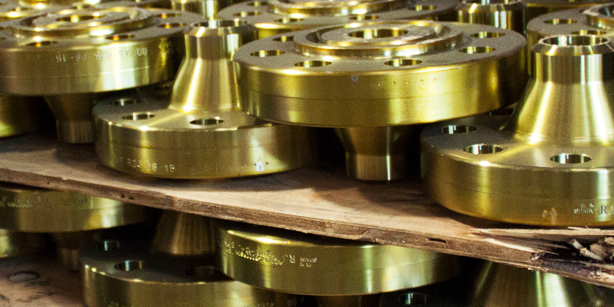 Gold carbon steel API flanges arranged in stacks inside a warehouse.