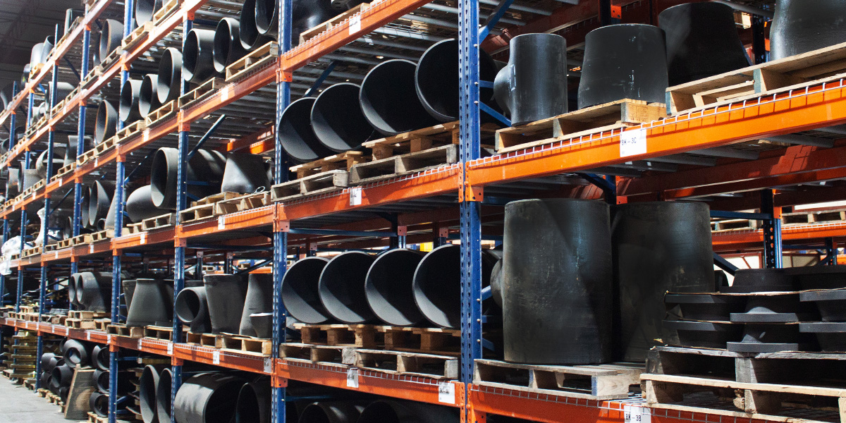 Carbon steel fittings neatly arranged on metal warehouse racking structure.